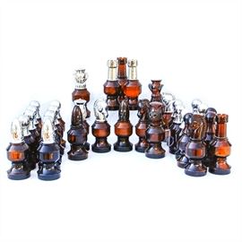 Collection of Avon Chess Piece Bottles: A collection of Avon chess piece bottles. The collection consist of a complete chess set with thirty-two pieces. All of the bottles are brown glass. The lids to the bottles are in brown and silver tone plastic.
