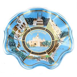 Vintage Disneyland Candy Dish: A vintage Disneyland candy dish. The candy dish is a wavy glass design in blue. Details of Disneyland are featured in sections throughout the dish including Frontier Land, Fantasy Land, Tomorrow Land, Main Street U.S.A., Adventure Land, and New Orleans square. Sleeping Beauty’s castle is featured in the center of the dish.