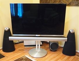 Lot 3: A Bang & Olufsen BeoVision 7-55 TV and Sound System. The television measures 64" from corner to corner, and includes a sound bar, remote and stand. The label on the reverse reads: Type #9489, Item #1846177, Serial #21826734. Together with 2 BeoLab 3 speakers on stands (Item #1216511, Serial #20078189); 2 BeoLab 9 speakers, cone shape (Type #6217, Item #1621700, Serial #20691292); 1 BeoLab 2 subwoofer (Type #6863, Item #1680003, Serial #21872589); and 1 storage cabinet, 24 1/2 x 17 1/2 x 19 1/2" high. Good, used condition. ESTIMATE $ 2,000-3,000