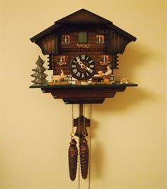 Lot 63: A contemporary Black Forest cuckoo clock. Chalet with seated man holding mug of beer, with pendulum and two pinecone weights. One weight chain is inoperable, possibly just off track. 10 1/2" wide, 15" high to the pendulum. ESTIMATE $100-200