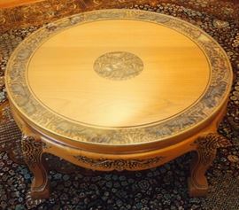 Lot 37: An Indonesian carved wood cocktail table. Round, carved in relief at the center and about the edge with elephants among foliage, raised on four shaped legs with floral carved knees. Several minor scuffs to the feet; overall, good condition. With plate glass top. 36 x 16" high. ESTIMATE $300-500