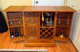 Lot 47: An Indian carved wood bar cabinet. Rectangular with hinged top opening to extended surface, above a pair of doors opening to fitted interior, two drawers and a cabinet. The exterior carved in relief with birds perched on flowering branches. A few very small and minor scratches due to use; overall, good condition. 30 x 20 x 37 1/2" high, closed. ESTIMATE $200-300 *Lot does not include contents of the cabinet.