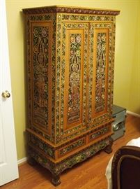 Lot 39: An Indonesian carved and polychrome wood cabinet. A pair of doors opening to storage shelves, two drawers at the base. Carved figural panels bordered by flowers, raised on mask feet. Two cracks noted to the top, approximately 11" and 17" long. 36 x 20 x 65" high. ESTIMATE $300-500