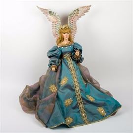 House of Faberge Franklin Heirloom "Angel of Hope" Porcelain Doll: A House of Faberge Franklin Heirloom “Angel of Hope” porcelain doll. The doll features bisque hands and a head with blonde hair and blue eyes. She wears an elaborate blue gown trimmed with a gold cross stitched pattern around the waist extending to the base of the dress. The Dress also features a gold tone foliate design accented with white gemstones. A gold crown with white gemstones sits atop her head and a pair of porcelain angel wings with a feathered texture. The doll is marked “House of Faberge” on the back of the neck.