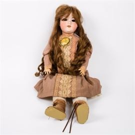 Antique Armand Marseille Porcelain Doll: An antique Armand Marseille porcelain doll. This doll has a bisque head and composition arms and legs. She wears a mauve colored vintage dress with lace applique along the front and a yellow floral and white bead brooch. Pantaloons and lace-up boots complete the costume. Marked “Armand Marseille Germany 1390/A/642/M.”