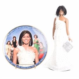 Danbury Mint "Michelle Obama" Inaugural Doll and Commemorative Plate: A Danbury Mint Michelle Obama Inaugural porcelain doll and Michelle Obama plate. The doll comes in the original box and is marked and labelled. This piece shows Michelle Obama wearing the white gown worn for the 2009 Inaugural Ball. The plate is marked “Michelle Obama: Elegance, Style and Grace Danbury Mint MBI” and “A 1550” and depicts Mrs. Obama in various outfits.