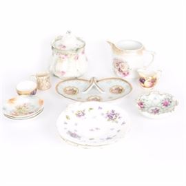 Collection of Porcelain Tableware: A collection of porcelain tableware. The group includes a white tea pot with floral motifs marked “284,” a small floral bowl marked “Germany,”a floral dish with three feet, not signed, a candy dish with figures marked “8329,” and a floral lidded container marked “Russia”. Also included is a small creamer with a figure and a gold rim marked “Saoler,” a small creamer and sugar dish with fruit pattern marked “Aynsley England,” a pair of small floral dishes marked “Schumann,” and a pair of white plates with purple violets, not marked.