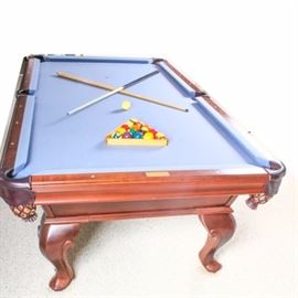 Olhausen Billiard Table: An Olhausen billiard table. This slate billiard table is topped in a grey-blue felt with leather side pockets, pearlized sights, Virginiana legs with an eclipse apron. The table appears to be mahogany and of the Virginian style. This lot includes 7 pool cues, 2 racks and assorted billiard equipment.