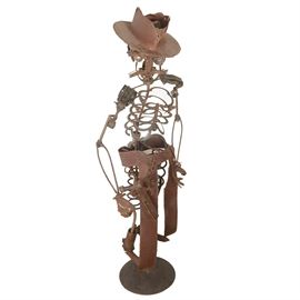 Large-Scale Salvaged Metal Sculpture Of Skeletal Sheriff: An original salvaged metal folk art sculpture constructed in the style of contemporary folk artist Dan Klennert, depicting a larger-than-life skeletal sheriff figure created with re-purposed materials, including twisted metal cable, car springs and bearings, chain, gears, laser-cut and welded metal. The sheriff is displayed on a round metal stand with armature and wire anchors. The sculpture can be dissembled for easier moving as the hat, head, shoulders and arms, chaps and legs, pistol, holster, and armature are separate. A wonderful piece which could be used indoors or in a garden sculpture.