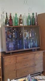 Decorative bottles in all shapes, colors and sizes displayed in a beautiful mid-century china cabinet.