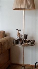 Whimsical goat figurine displayed on a brass lamp/table with some vintage silver-plated pieces.