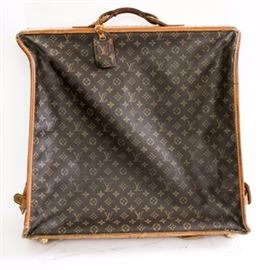 Louis Vuitton Garment Bag Suitcase: A Louis Vuitton garment bag. This brown monogram canvas garment bag has tan leather edges and trim, including snap straps on either side to secure the bag in folded position. The bag features zipper pockets as well as an exterior zippered pouch secured by hanging clips, a separate interior zipper pouch and several coat hangers. The top of the suitcase under the handle is engraved with the personal initials R.I.B.
