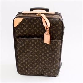 Louis Vuitton Wheeled Suitcase: A Louis Vuitton wheeled suitcase. This case has the Louis Vuitton patterning along the exterior as well as several tags with “Louis Vuitton” along the exterior. There is an extendable handle for rolling purposes, and along the interior is a clothes hook and a zipper along the bottom for further storage. This bag is marked to be from France.