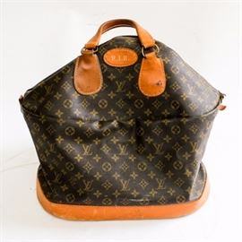 Vintage Louis Vuitton Carry-On Bag: A vintage Louis Vuitton carry-on bag made under license in the United States by The French Company. This brown monogram canvas bag features tan leather trim and a Talon zipper closure. A tag reads, “Louis Vuitton Paris, France Manufactured by The French Co. U.S.A. Under Special License.” A round leather patch just under the handles is marked with the personal monogram, R.I.B.