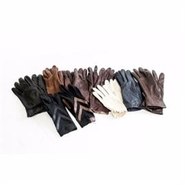 Collection of Women's Driving and Fashion Gloves: A collection of women’s driving and fashion gloves. This includes seven matching pairs and two unmatched gloves. Included are six pairs in black, brown, navy blue and burgundy leathers. A pair of winter white gloves included feature a gather wristband. Two Isotoner gloves in a similar style with different colored leather trimming are included.