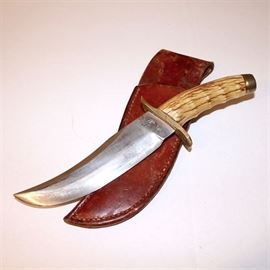 W.F. Moran Vintage Bone Handle 7" Lime Kiln Knife with Leather Sheath: A vintage W.F. Moran 7" lime kiln clip point blade with stag handle knife and custom stitched leather belt sheath. Knife features a brass cross guard and carved grip handle with metal pommel for hammering. This circa 1960s fixed blade hunting knife is heavy and substantial, created by William (Bill) F. Moran Jr. (1925-2006) who was a pioneering American knife maker. He founded the American Bladesmith Society and is notable for reintroducing the process of making pattern welded steel to modern knife making. Moran’s knives have been especially sought after by celebrities and heads-of-state. The ricasso is stamped “W.F. Moran Lime Kiln MD.” on one side.