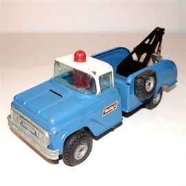 Vintage "BuddyL" Blue Wrecker Truck: A vintage “BuddyL” wrecker truck painted blue with white cap roof and red emergency light casing. Truck has a galvanized metal front grill piece, rubber tires with a flat spare hanging on one side of the truck bed, and a black painted winch craned in the truck bed with large end hook. Red “Buddy L” brand stickers are affixed to the cab doors on both sides.