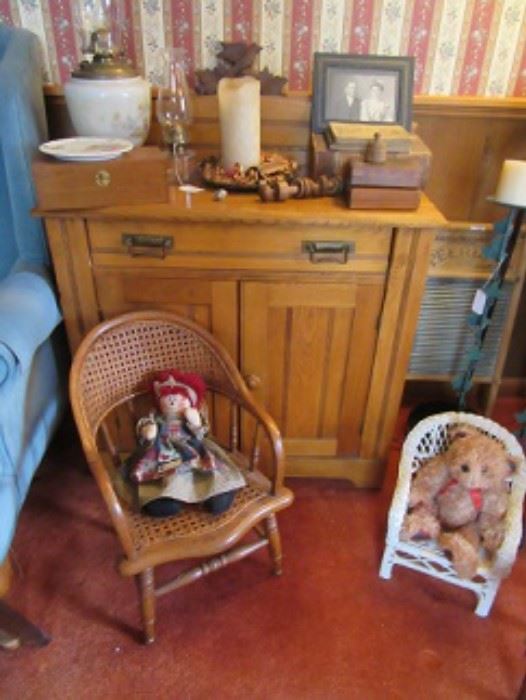 Pine wash stand with oil lamps, wood boxes, and framed early photo. The child's chair has a raggedy ann doll and the doll chair has a bear sitting in it. 