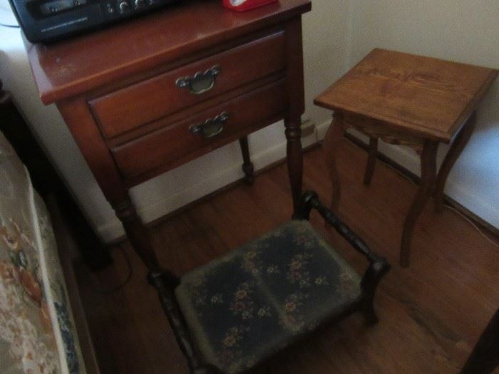 Two drawer night stand in the room with a double bed. The plant stand on the right is oak. The foot stool is in front of the table. 