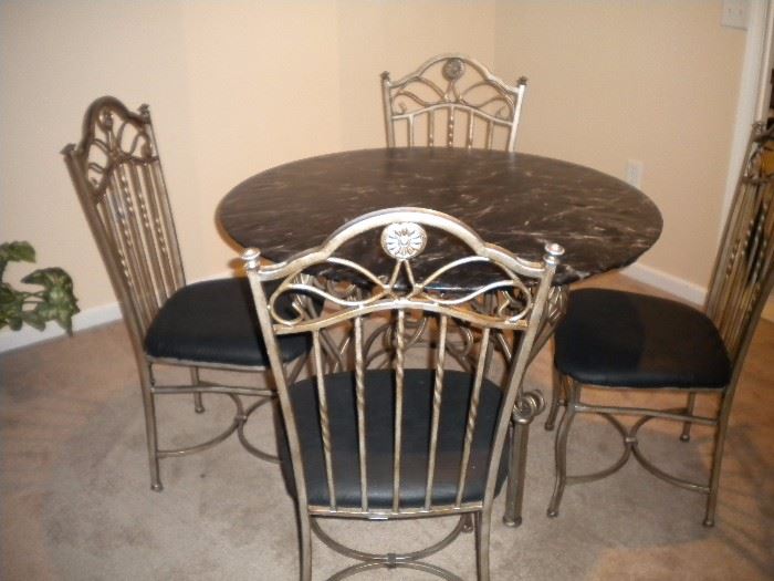 Glass top wrought iron table and four chairs, has black marble look cover