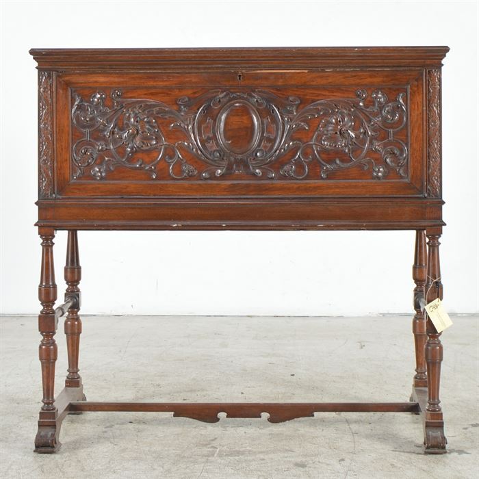 Victorian Gothic Revival Carved Walnut Writing Desk: A Victorian Gothic Revival writing desk in walnut. The front is heavily carved and opens out to reveal a fitted interior with drawers and shelves inside. There is a keyhole escutcheon but no key. The legs are turned with two turned side supports. The bottom sides are connected a by a shaped H stretcher atop scrolled feet.