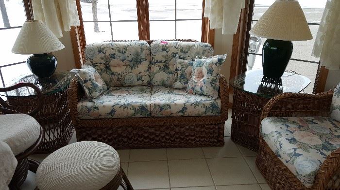 Wicker set includes love-seat, chair, and two end tables along with floral cushions and pillows 