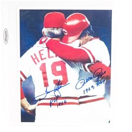 Pete Rose and Tommy Helms Signed Cincinnati Reds Lithograph: A Pete Rose and Tommy Helms signed Cincinnati Reds lithograph. It depicts Rose hugging Helms upon breaking the home run record in 1985. The figures are hand signed with each player’s respective signature, along with the year each received Rookie of the Year. The piece comes in a clear plastic sleeve with a Classic Moments Certificate of Authenticity.