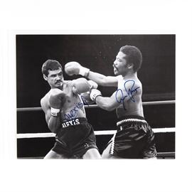 Aaron Pryor and Alexis Arguello Signed Orange Bowl Boxing Match Lithograph: An Aaron Pryor and Alexis Arguello signed boxing match lithograph. The black and white image depicts the legendary bout between the two boxers at the Orange Bowl stadium in 1982. Both figures are signed by the respective pugilists. The piece includes a Classic Moments certificate of authenticity, as well as images of the the boxers, in a plastic sleeve. Both Alexis Arguello (1952-2009) and Aaron Pryor (1955-2016) are ranked among the greatest fighters of all time.