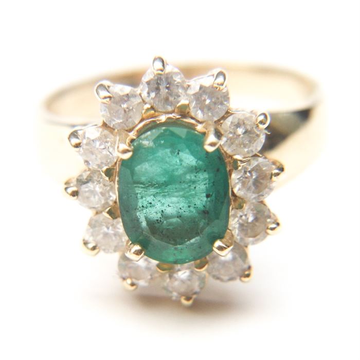 14K Yellow Gold Emerald and Diamond Ring: A 14K yellow gold ring. This ring features a smooth shank leading to an oval emerald centerpiece bordered by a line of round natural diamonds in prong settings.
