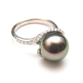 Mikimoto 18K White Gold Pearl and Diamond Ring: An 18K white gold ring by Mikimoto. This ring features a smooth band leading to twisted shoulders ornamented with round diamonds in prong settings and holding a Tahitian black pearl centerpiece.