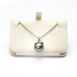Mikimoto Gray Pearl and Diamond Pendant Necklace: A Mikimoto gray pearl and diamond pendant necklace. The piece features a sphere shaped grey pearl at the center with strands of diamonds surrounding the top of the pearl. It sits along a silver tone chain link necklace that is marked “750”.