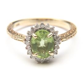 14K Gold Ring With Peridot and Diamonds: A 14K yellow gold ring with a foliate shank leading to an oval cut center peridot, surrounded by full cut diamonds.