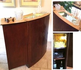 Turnidge of London Mid Century teak wood bar. Space saver design allows top and sides to fold out, revealing a glass serving surface. Interior of bar has a working electric light. Interior base has metal lined holes for wine or spirits bottle storage. Vintage glass bar ware including ice bucket with tongs, decanter with stopper, nut dish and old fashioned glasses. 