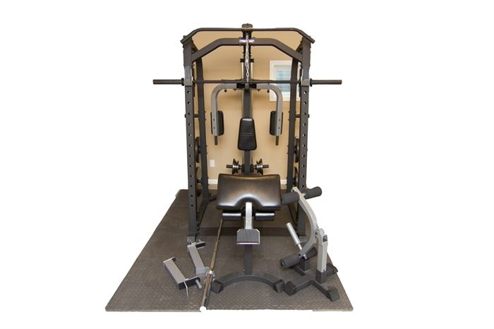 Fitness Gear Home Gym with Accessories: A Fitness Gear home gym with accessories. It features a robust metal construction with multiple exercise components, including the butterfly press, leg curls, barbell squat, lat pull, and arm curl/rowing. Includes two barbells (one of which is attached) and 255 lbs of free weights. Comes with a rubber mat that can be taken apart.