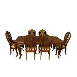 Parquetry Top Queen Anne Style Dining Table and Chairs: A parquetry top Queen Anne style dining table and chairs. The wooden table features a bisected rectangular top with chamfered corners and four pairs of cabriole legs with floral relief carvings. Light brown trim lines the perimeter of each table section. Includes a 20-inch wide leaf, which increases the table depth from 82 to 102-inches. The eight chairs feature an open back rest with a carved relief shell finial and a swirling floral splat, a cushioned seat, and four legs, two of which have matching floral relief carvings. Both the table and chairs have a dark brown finish with gold tone highlighting on the floral elements. The seats are covered with a floral beige upholstery.