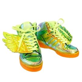 2014 Jeremy Scott Adidas Iridescent Gold Foil Wings Sneakers: A pair of 2014 Jeremy Scott for Adidas Iridescent Gold Foil Wings sneakers. This pair of Adidas sneakers from Jeremy Scott features a metallic gold tone foil wing design. The hi-top sneakers have an iridescent gold, purple, green, blue and orange design with white laces.