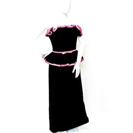 1985 Victor Costa Velvet Evening Dress: A 1985 Victor Costa velvet evening dress. The dress is a black velvet evening gown that features a strapless top with pink trimmed ruffles, a pink belt with a bow and a pink pleated trim on the waistline. The dress has a zipper on the back, straight line skirt and a deep pink lining. The label inside reads “Victor Costa”