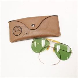 Vintage Bausch and Lomb 12K Gold Filled Ray Ban Aviator Sunglasses: A pair of vintage Bausch and Lomb 12K gold filled Ray Ban aviator sunglasses. The pair of glasses are green tinted lenses in a gold filled frame with a yellow enamel bridge and nose guards. The glasses come with a brown case with a front snap and both glasses and case are labeled “Ray- Ban”.