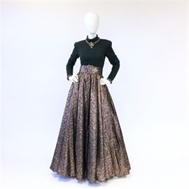 1980's Victor Costa Evening Gown: A vintage circa 1980 Victor Costa evening gown. The gown features a fitted long sleeve heather grey knit bodice with a mock turtle neck, a full floor length brocade skirt and wide fabric belt. A matching necklace is crafted of braided skirt fabric and accented with faux gemstones. “Victor Costa” is labeled to the interior. A length of additional skirt fabric is included.