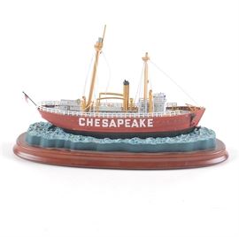 Danbury Mint "Lightship Chesapeake" Model: A model ship from the Danbury Mint. This model is of the ship Lightship Chesapeake and is supported on a water current; with the boat and water being composed of painted resin. The model is held on a polished wooden stand that is cherry wood in tone and features the ship’s name and maker’s mark on the bottom of the base in gold tone writing.