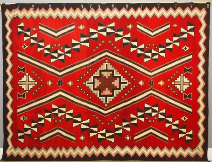 An 11.1 x 8.4' circa 1930 Navajo Ganado regional rug.  Woven of handspun wool, in natural white, black, gray, dark brown and light brown on a red ground, with three serrated diamonds along the center flanked by angular bars and serrated devices, within a serrated border.  Light wear; several stains.  133 x 100".  ESTIMATE $6,000-8,000  Provenance:  Commissioned by John C. Holley, Jr. of Grosse Pointe, Michigan from the Hubbel Trading Post, circa 1930, for use in his hunting lodge near Lake Placid, New York.  Christopher Selser of Park Avenue, New York, the former Director of ACA American Indian Arts who, along with Alice Kaufman, authored "Navajo Weaving Tradition: 1650 to the Present".  Purchased by Robert Teeter, June 1983.  The original correspondence between Teeter, Kaufman and Selser, pertaining to this item, is available for review.  