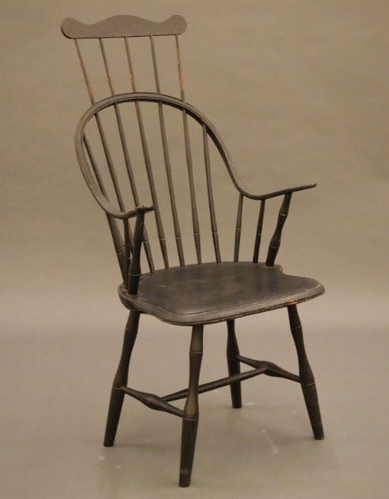 A late 18th/early 19th century New England continuous arm, comb back Windsor armchair.  Seven spindle back, shaped hand holds, turned spindles, shaped plank seat and turned stretcher base.  Hickory and Maple construction with a Pine seat.  Older Black paint with some wear, crack in seat, feet ended out approx. 5".  20 1/2 x 17 1/2 x 44 3/4" high overall.  ESTIMATE $400-600