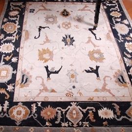 Hand Knotted Tufenkian Tibetan Area Rug: A hand knotted Tufenkian Tibetan wool area rug. This rug features a cream field with large palmettes in a palette of rose, gray, umber, and black. A resolved border displays the same color palette with a stylized herati pattern on a black field. The rug is finished with a white cotton warp fringe and has tags marked "Tufenkian Tibetan carpets are handknotted in the unique Tibetan loop-senneh style” to the reverse.