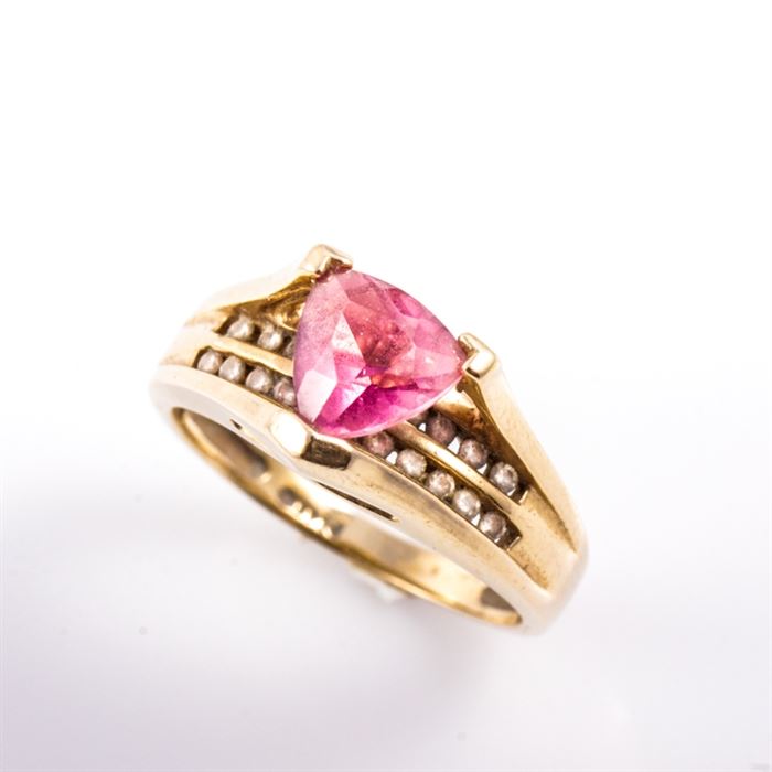 14K Yellow Gold, Tourmaline, and Diamond Ring: A 14K yellow gold ring featuring one center trillion cut pink tourmaline mounted in a high v-prong setting atop two rows of channel set round brilliant cut diamonds.