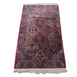 Macine Woven Karastan "Kirman" Area Rug: A machine woven Karastan “Kirman” area rug. This “Kirman” wool rug, which was made in the U.S., is rendered in a multi-hued palette of red, shades of pink, shades of blue, various greens, tan, taupe, mustard, and ivory. It features an allover design of lattice diamonds, which are populated with flowers, palmettes, and foliate shapes. The main border features a Herati pattern. The rug finishes in ivory applied fringe at either end and is marked on the reverse.