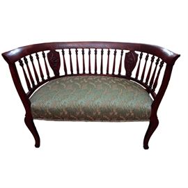 Antique Edwardian Style Settee: An antique Edwardian Style settee. This mahogany finished settee features an upholstered seat with a brocade fabric in a seafoam green color with ivory floral motifs. The curved back of this settee features turned spindles and two shield shaped splats with leaf motifs applied to them. This beautiful piece rest of two front cabriole legs and two back square splayed legs.