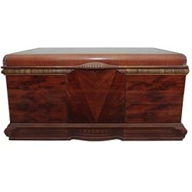 Art Deco Style Cedar Chest: An Art Deco style cedar chest. This cedar chest features a flat top with a rounded edge and beautiful Art Deco details like multiple wood veneers, like walnut and mahogany and rounded zebra wood molding, and circular carvings. The hinged lid features a carved handle and opens to a cedar lined chest with a felt lined shelf. This piece provides two keys for the lock.