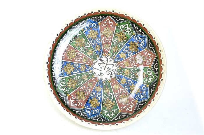 Early 20th Century Arabic Plate: An early 20th century Arabic plate. This plate features red, blue, and green underglaze painted patterns with Arabic writing at center. The underside is impressed with a stamp.