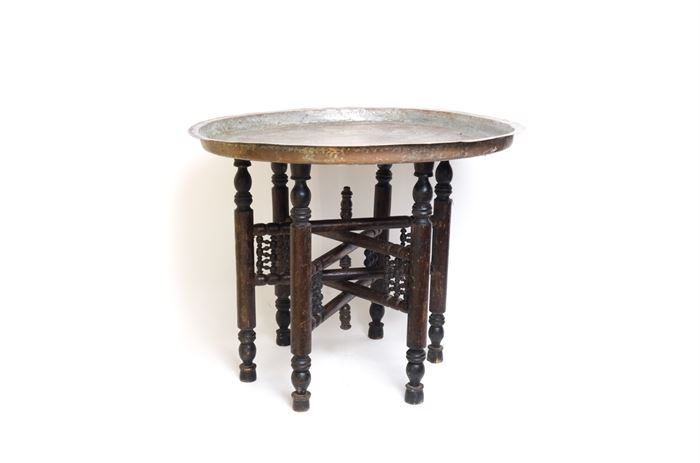 Turkish Tray Table: A Turkish tray table. A round tin over copper removable tray rests on a wooden stand. The plate is accented with engraved geometrical designs and shapes around the border. The legs of the stand are carved and are foldable.