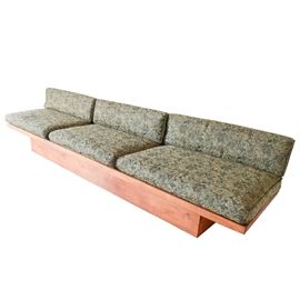Mid-Century Modern Otmar Platform Sofa: A mid-century modern wood platform sofa crafted by Otmar. The sofa has an overhung rectangular platform base with three loose back cushions and three loose seat cushions upholstered in a dense repeating floral pattern in greens, blues and taupe.